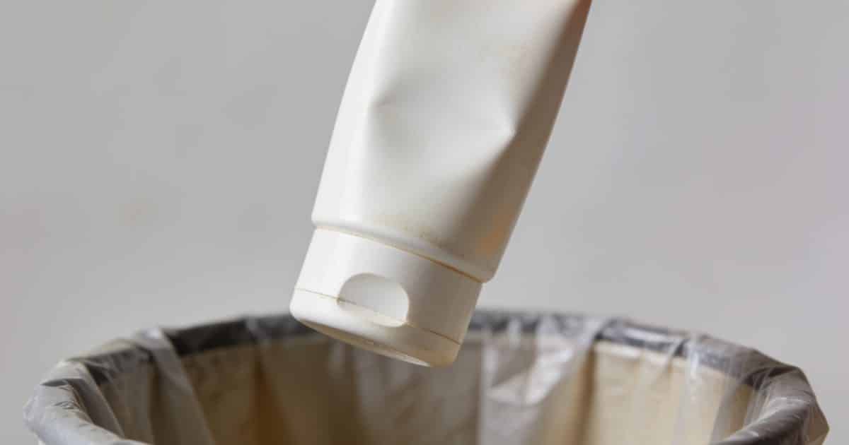 Bouteille de creme solaire vide tenue au dessus poubelle