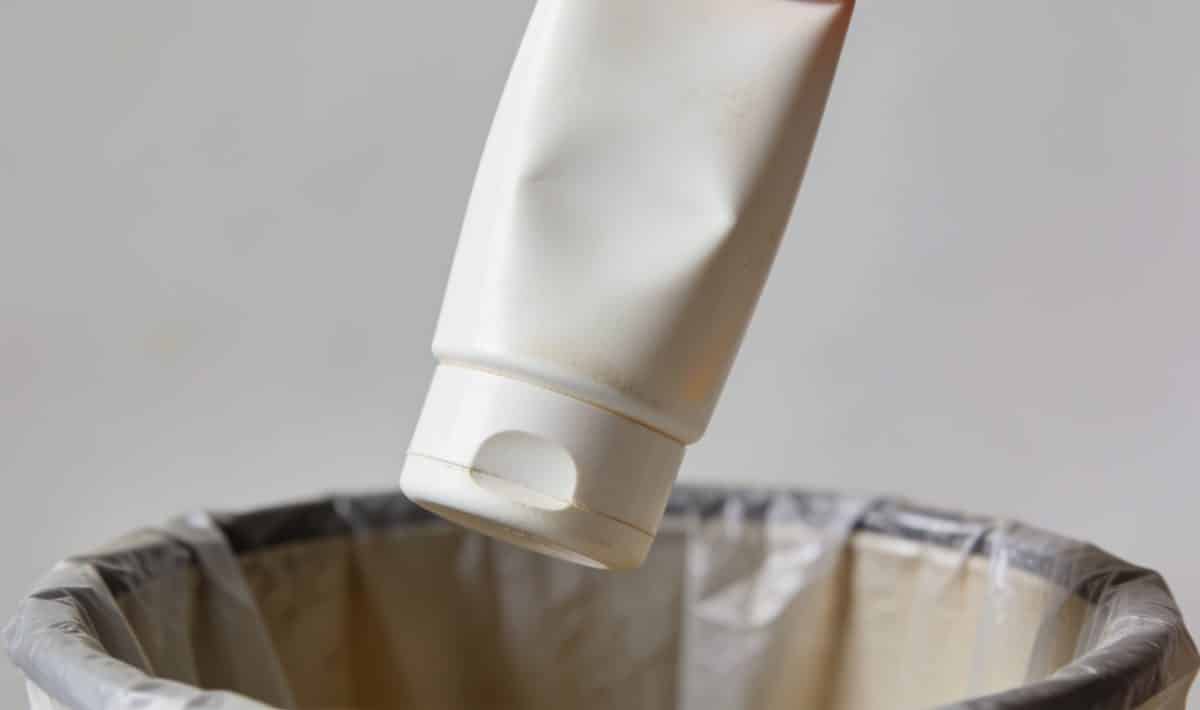 Bouteille de creme solaire vide tenue au dessus poubelle