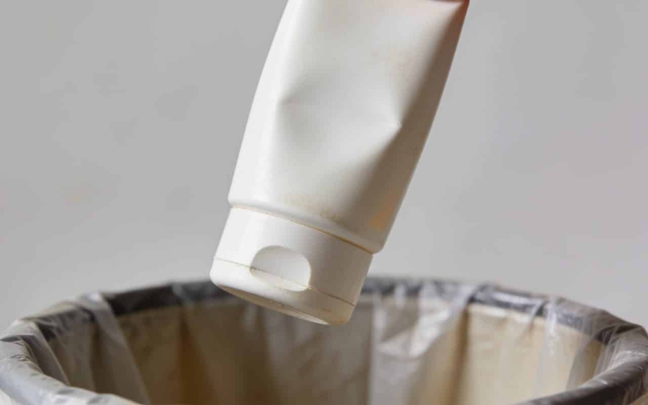 Bouteille de creme solaire vide tenue au dessus poubelle