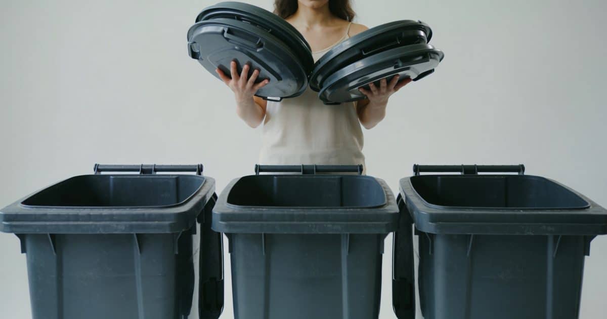 Femme debout tenant des couvercles devant trois poubelles