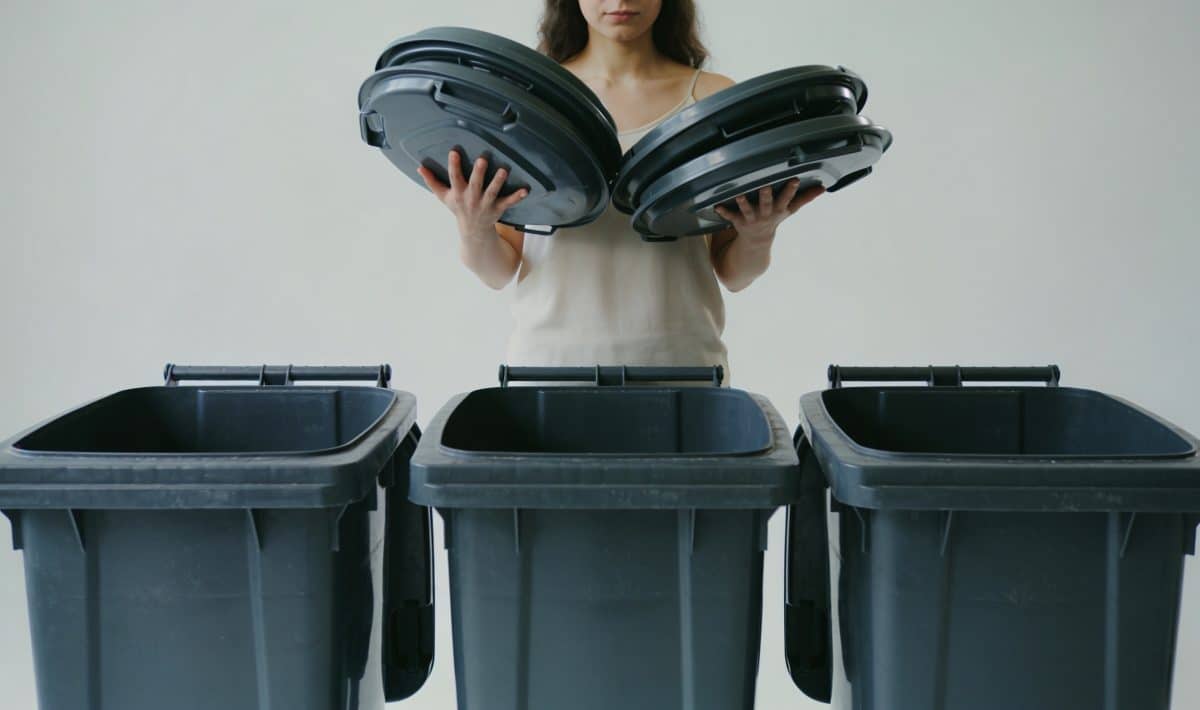Femme debout tenant des couvercles devant trois poubelles
