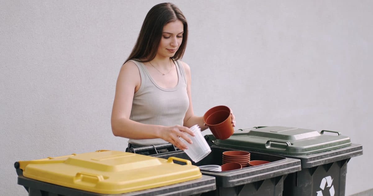 Femme debout triant pots de fleurs plastiques devant bacs de recyclage