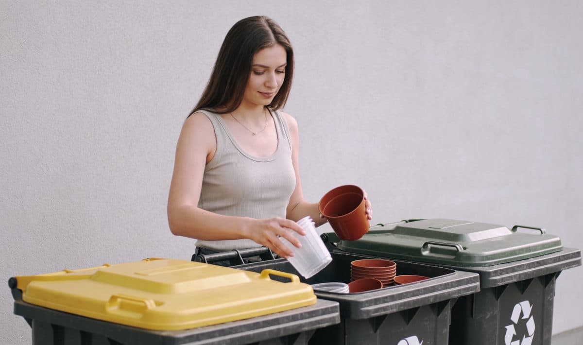 Femme debout triant pots de fleurs plastiques devant bacs de recyclage