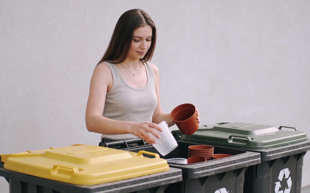 Femme debout triant pots de fleurs plastiques devant bacs de recyclage