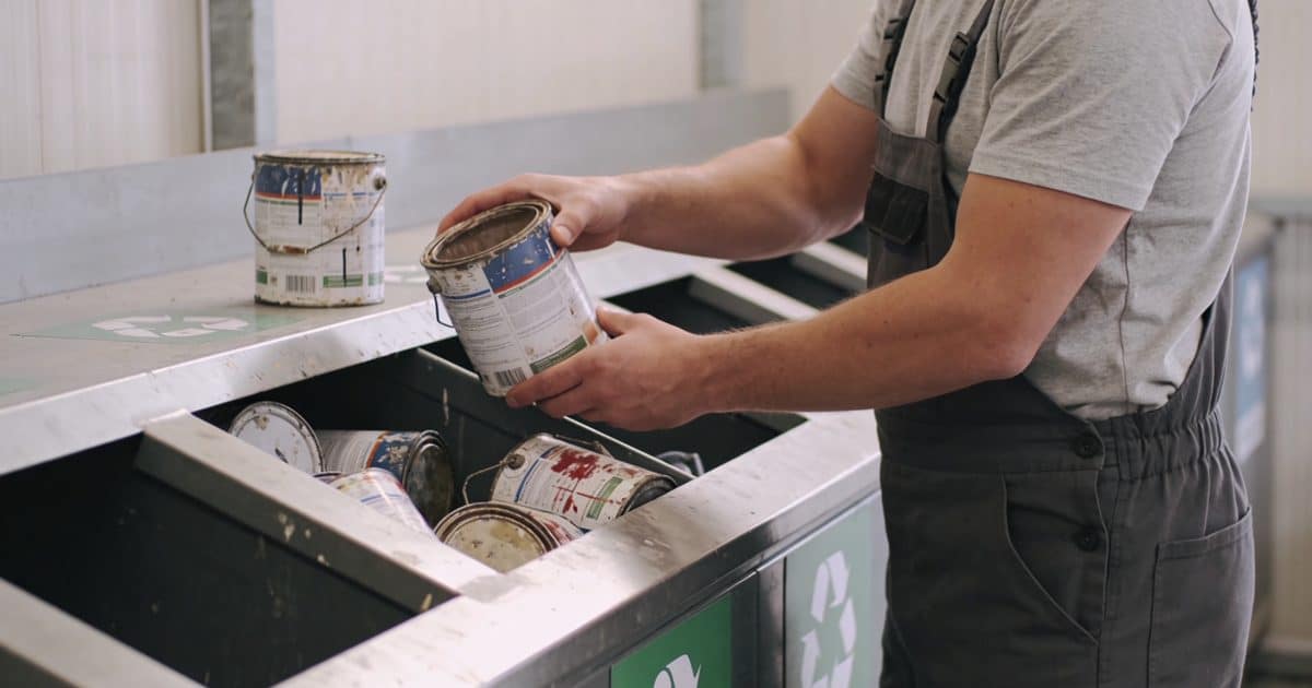 Homme depotant vieux pots de peinture en dechetterie