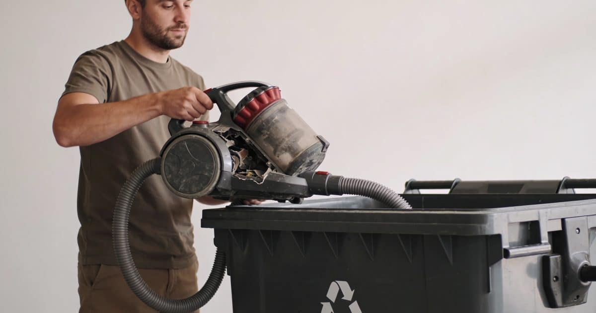 Homme depotant vieil aspirateur casse dans benne recyclage