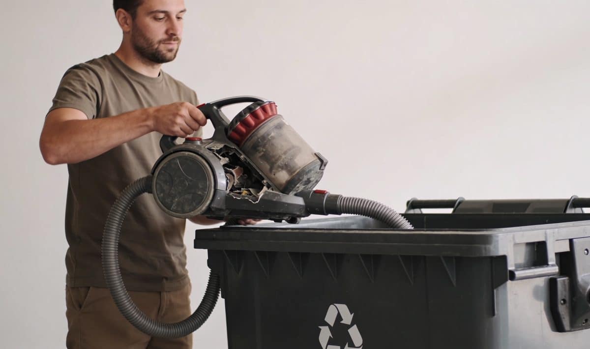 Homme depotant vieil aspirateur casse dans benne recyclage