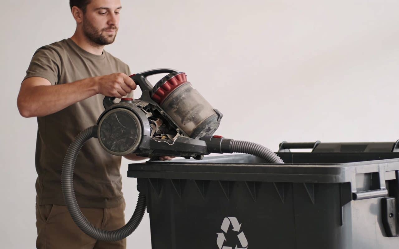 Homme depotant vieil aspirateur casse dans benne recyclage