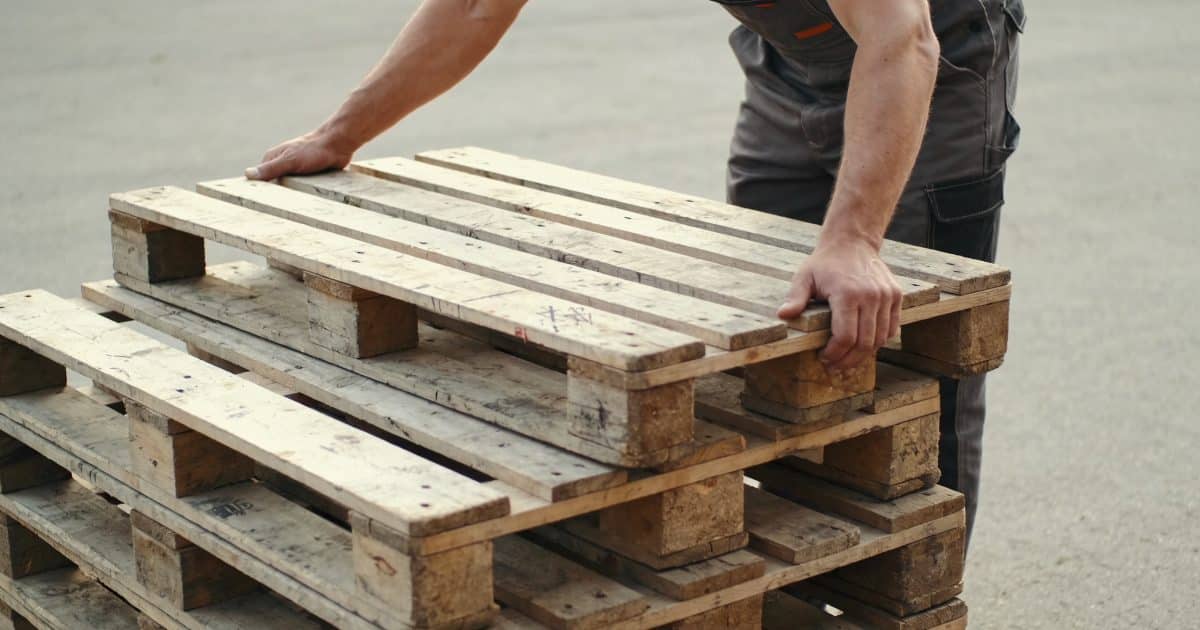 Ouvrier empilant des palettes en bois usees dehors