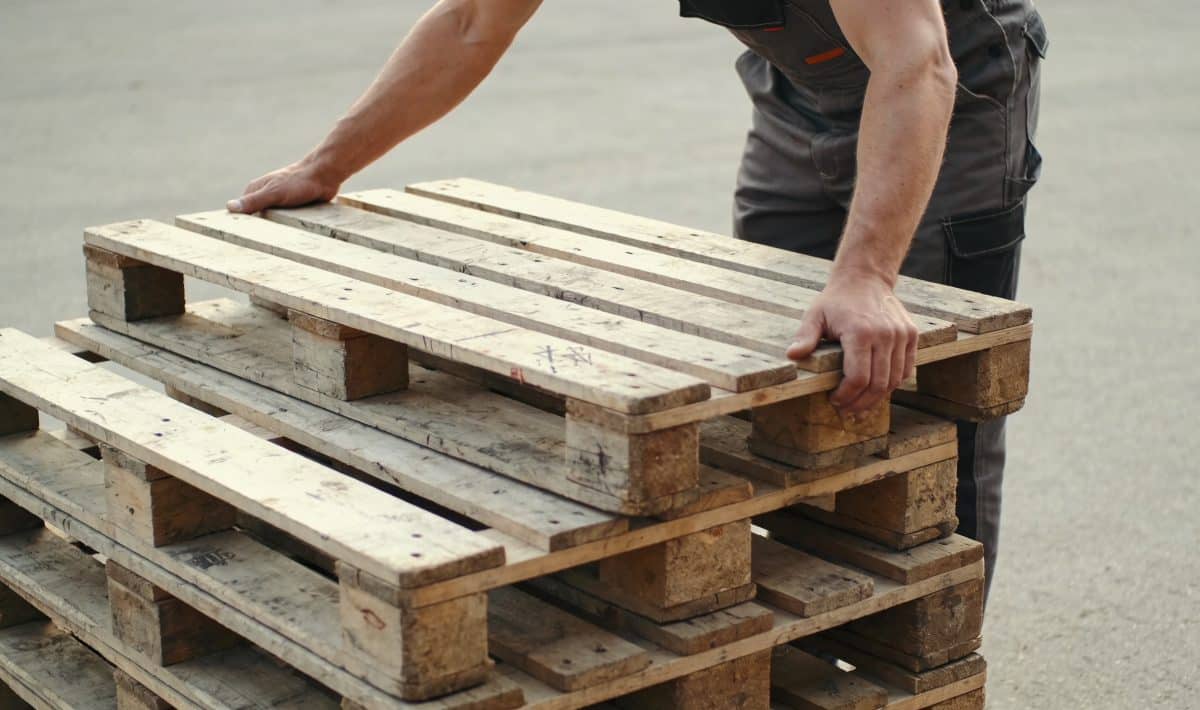 Ouvrier empilant des palettes en bois usees dehors