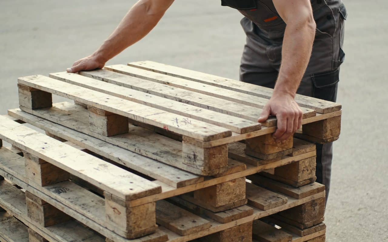 Ouvrier empilant des palettes en bois usees dehors