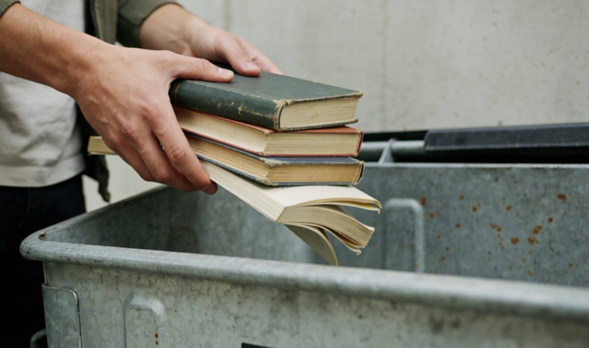 Personne deposant des livres uses dans une benne