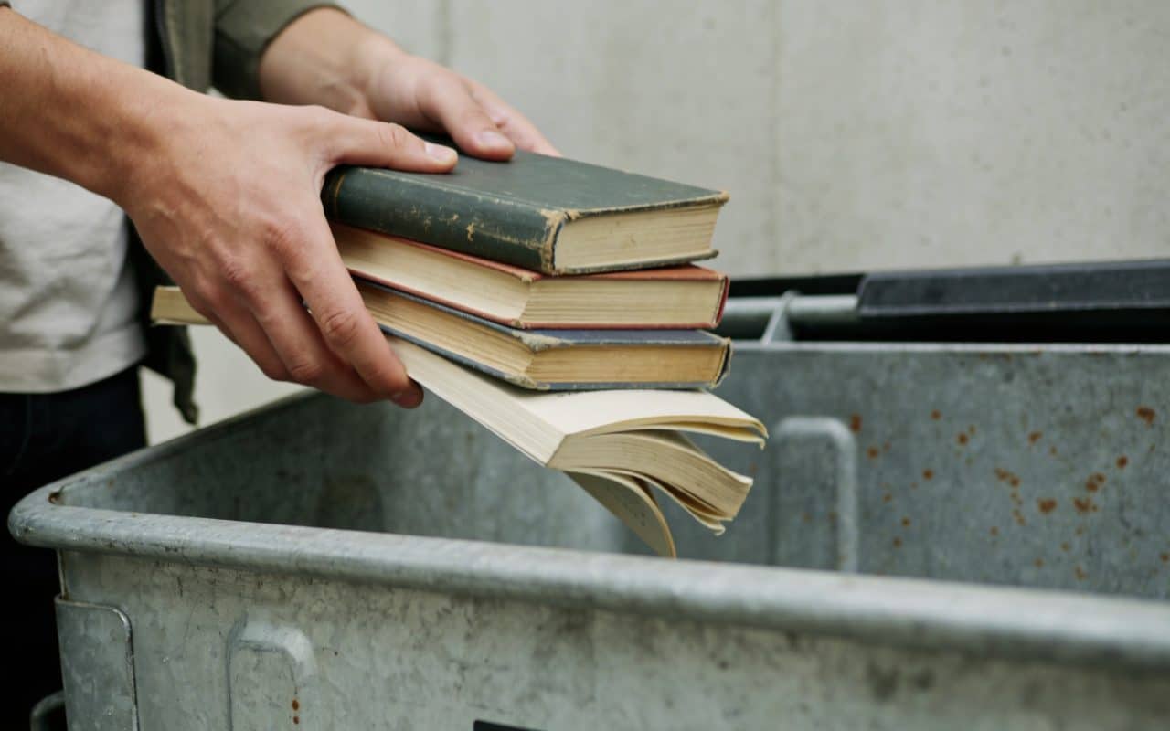 Personne deposant des livres uses dans une benne