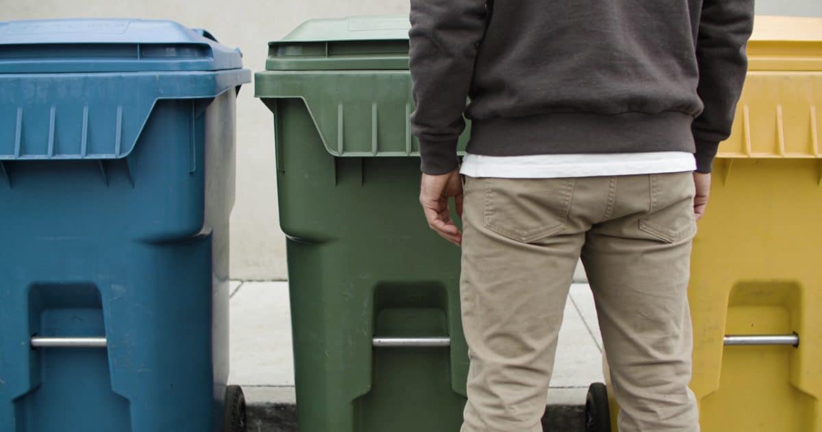 Personne devant trois poubelles de tri colorées