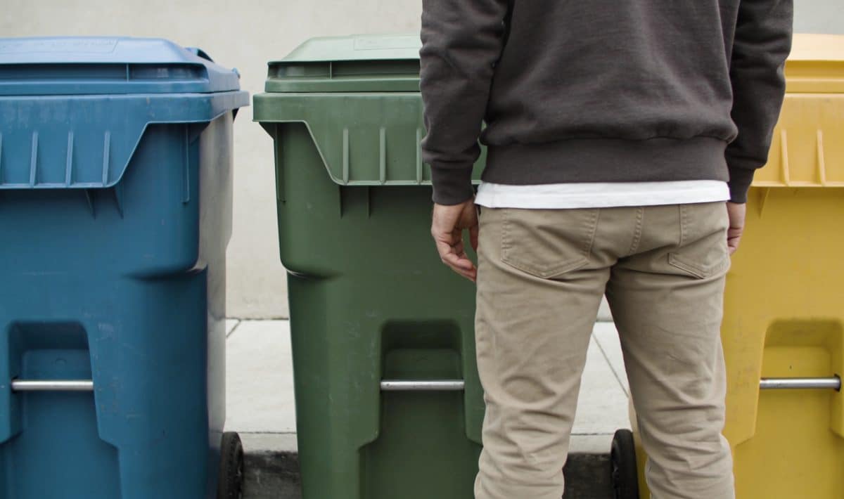 Personne devant trois poubelles de tri colorées