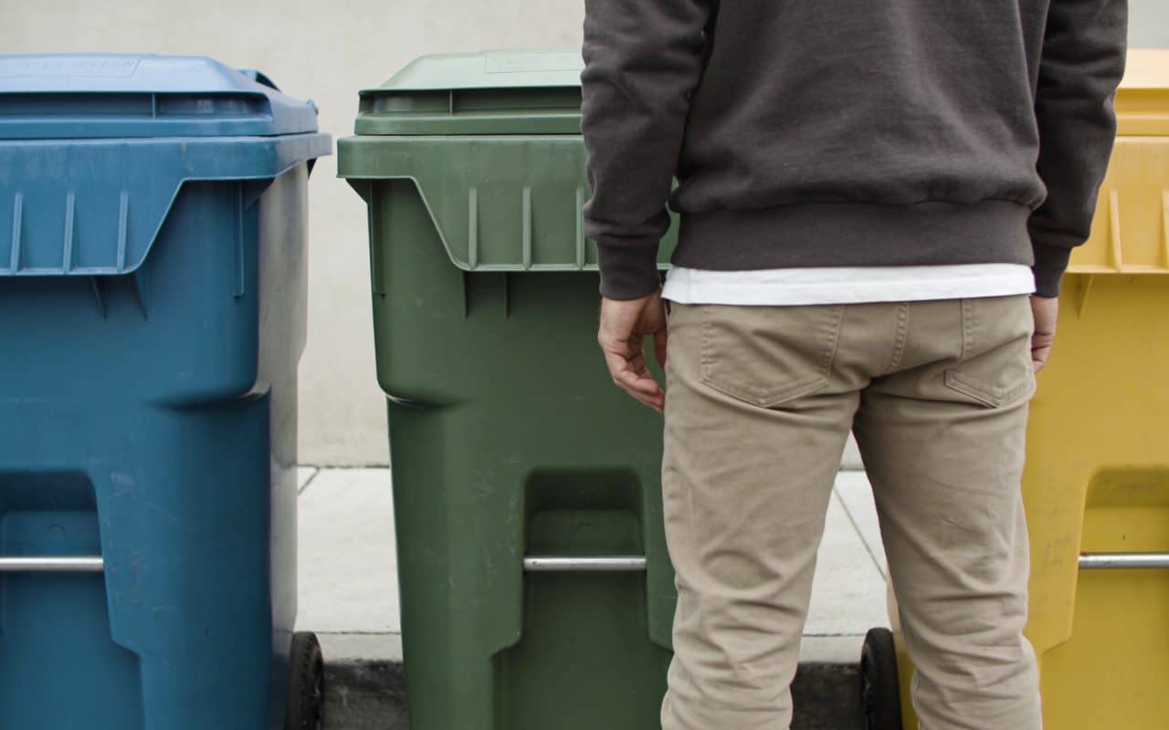 Personne devant trois poubelles de tri colorées
