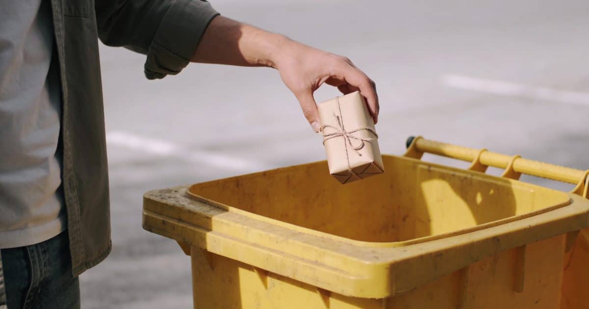 Personne jetant rouleaux de papier cadeau dans poubelle jaune