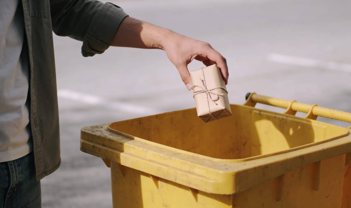 Personne jetant rouleaux de papier cadeau dans poubelle jaune