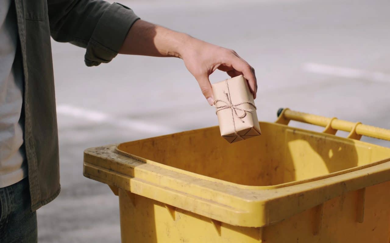 Personne jetant rouleaux de papier cadeau dans poubelle jaune