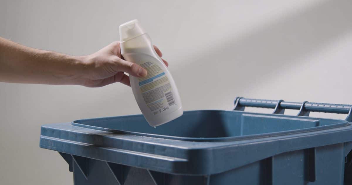 Personne jette une bouteille de shampoing pleine dans poubelle de tri