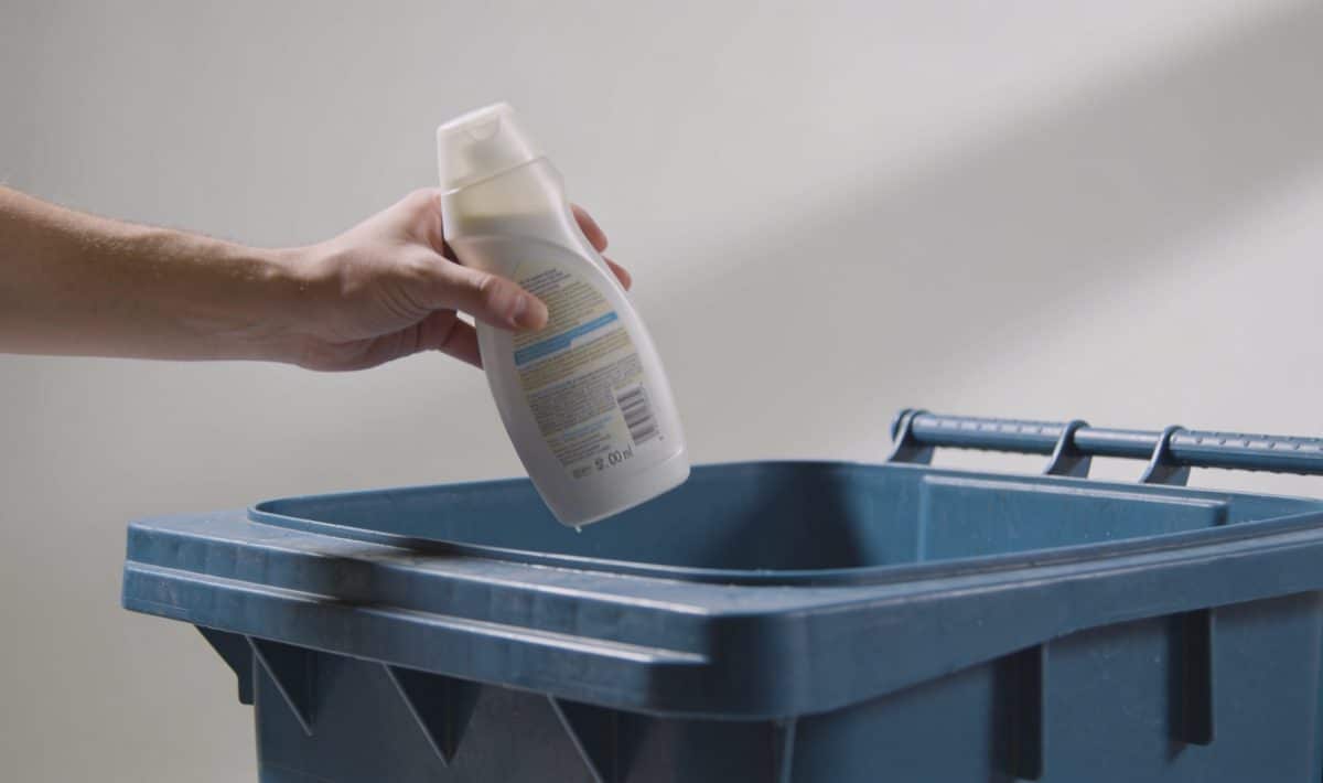 Personne jette une bouteille de shampoing pleine dans poubelle de tri