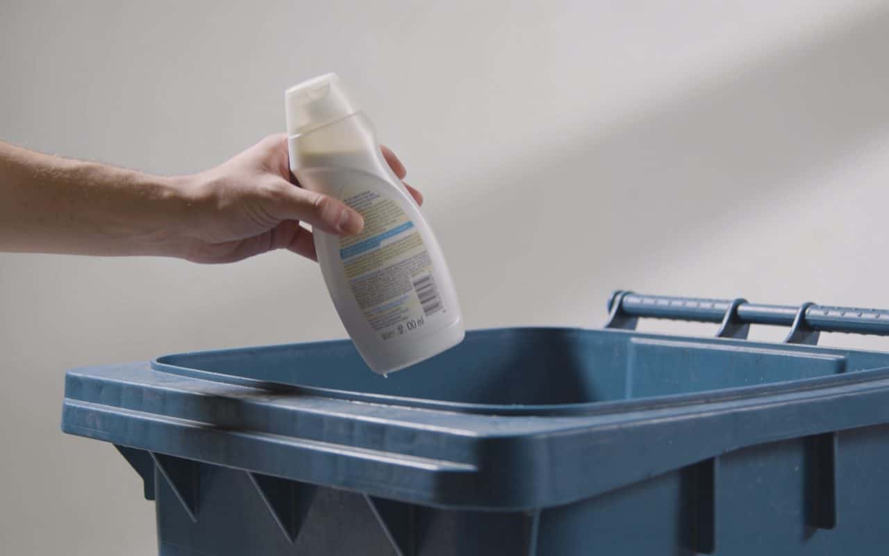 Personne jette une bouteille de shampoing pleine dans poubelle de tri