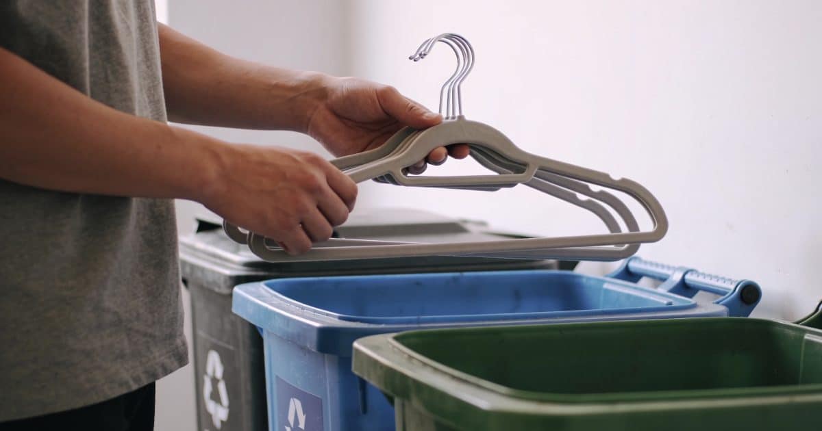 Personne triant des cintres devant poubelles de recyclage