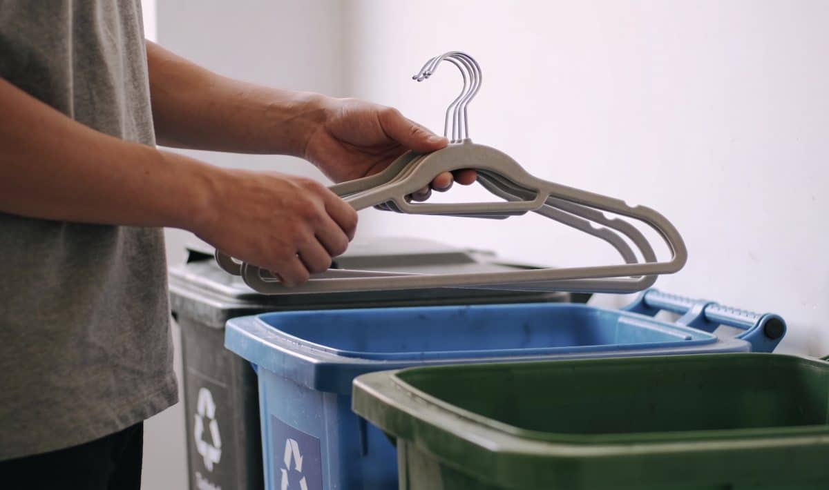Personne triant des cintres devant poubelles de recyclage