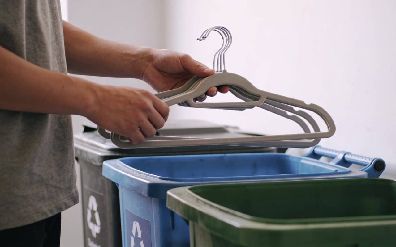Personne triant des cintres devant poubelles de recyclage