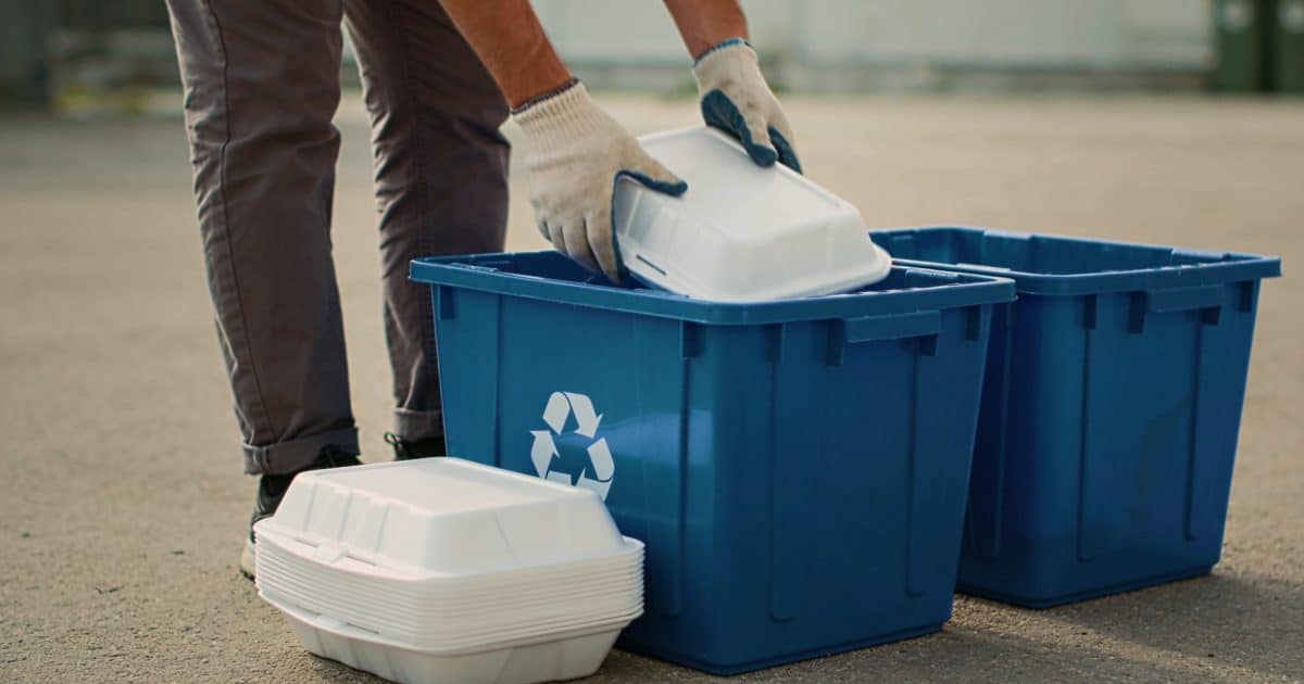 Personne triant des barquettes en polystyrene devant bacs de recyclage