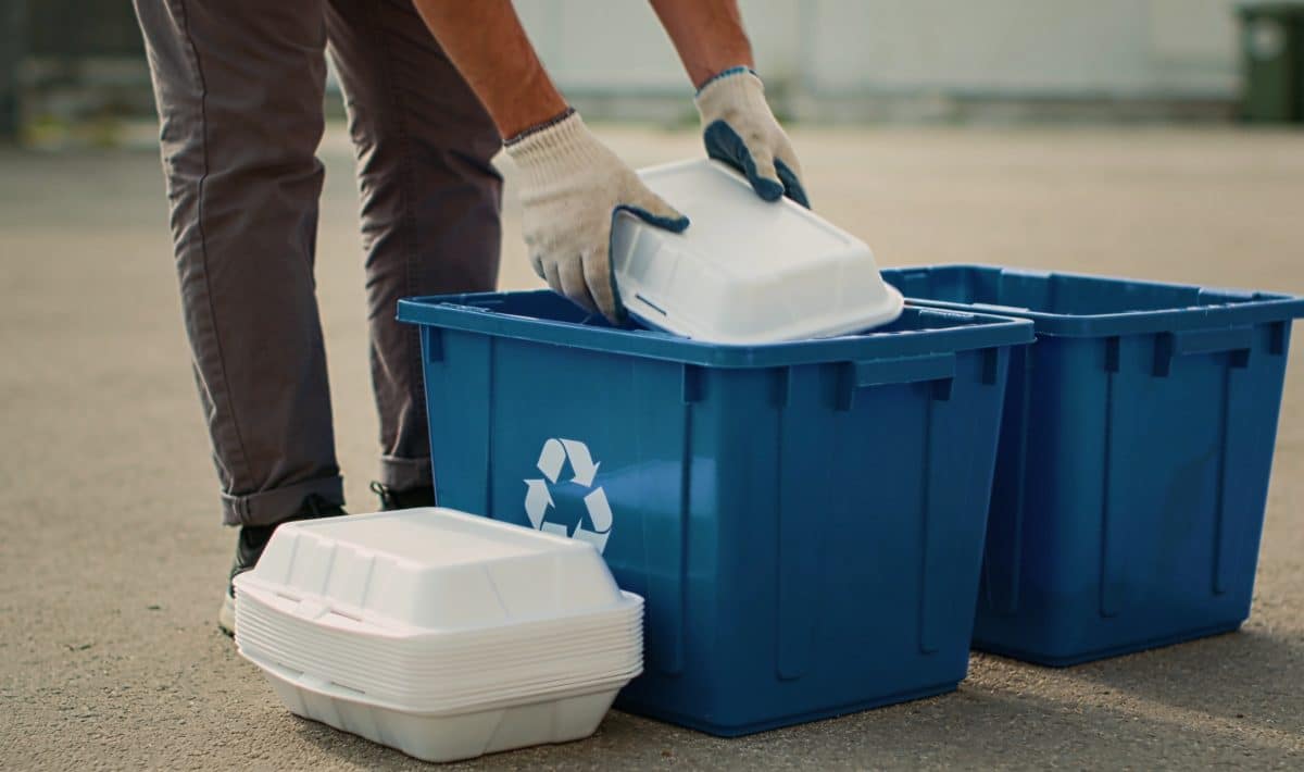 Personne triant des barquettes en polystyrene devant bacs de recyclage