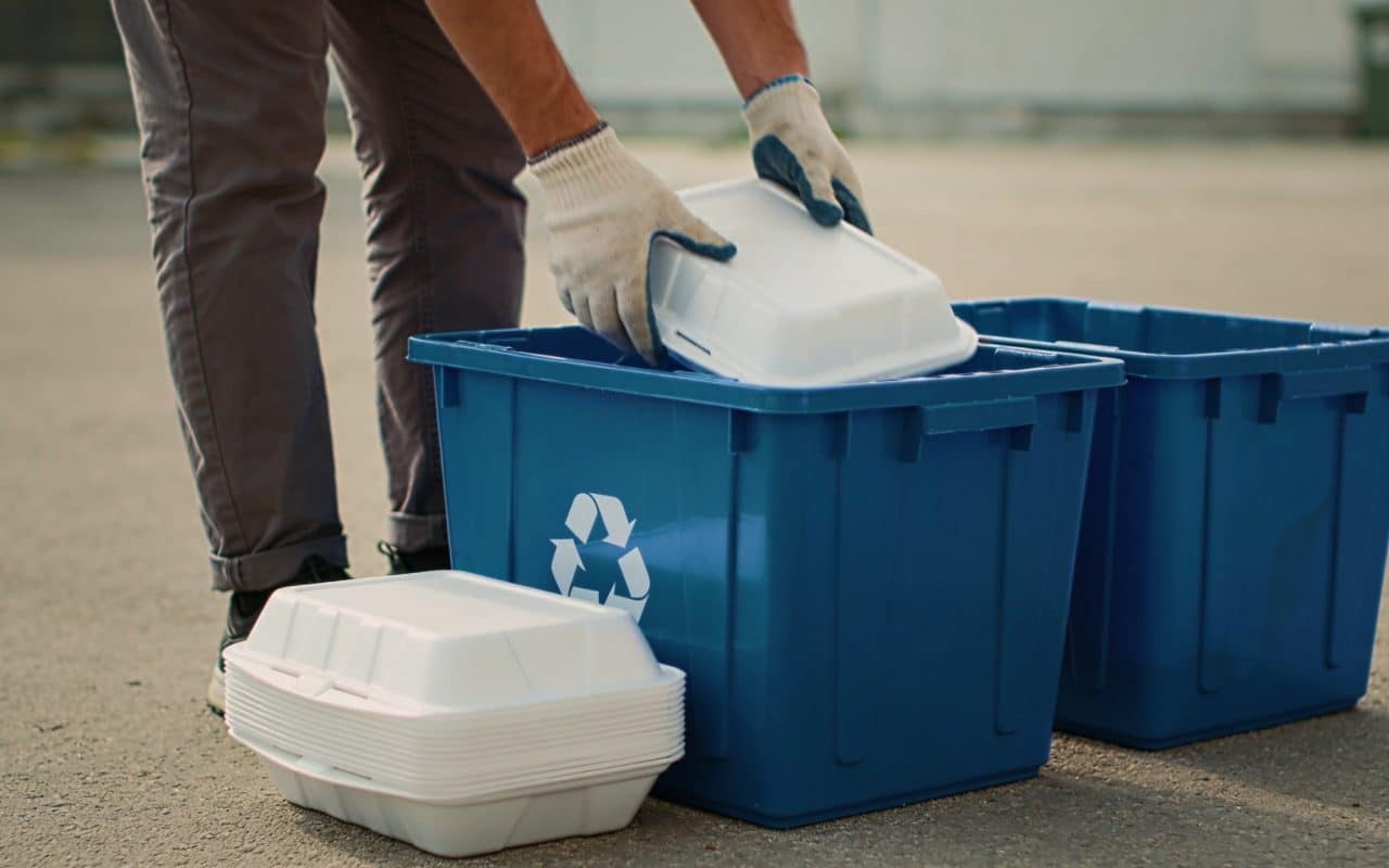 Personne triant des barquettes en polystyrene devant bacs de recyclage