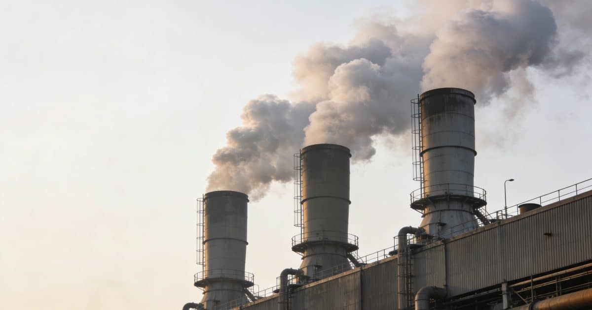 Usine fumante avec grandes cheminees rejetant epaisse fumee
