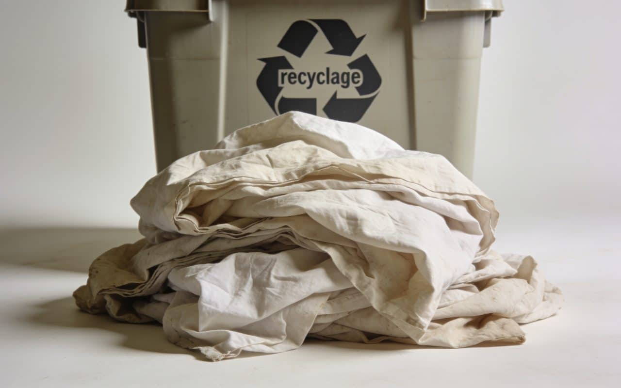 Tas de vieux draps froisses devant conteneur recyclage